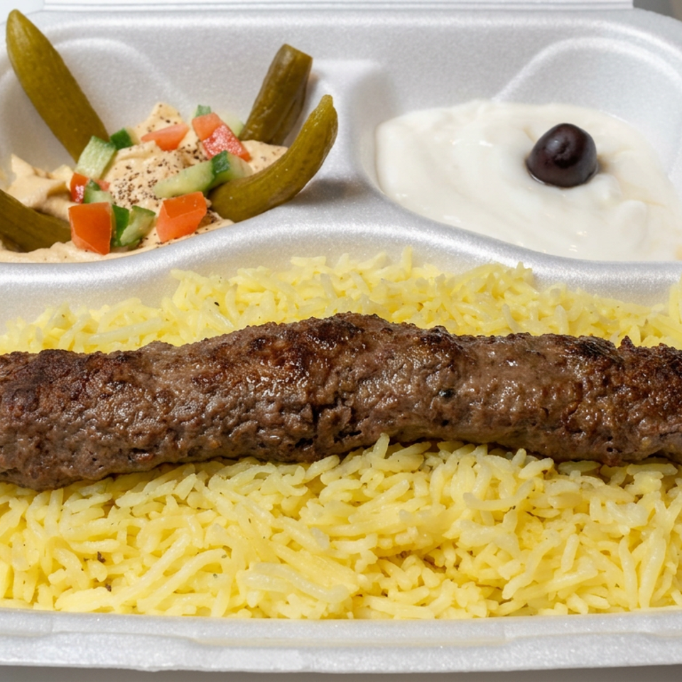 Grilled kofta served over yellow rice with hummus, pickles, chopped vegetables, and yogurt sauce in a divided takeout container.
